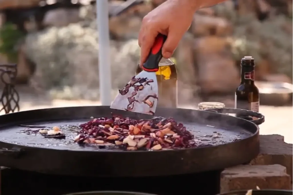 Dusenie červenej kapusty na liatinovom pláte nad ohňom